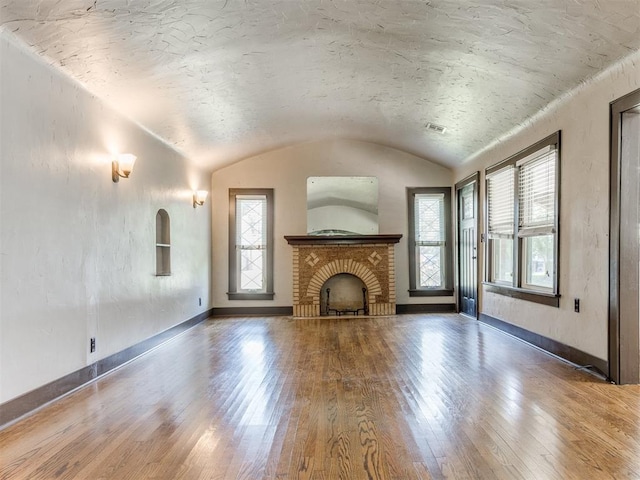 2420 NW 21st St, Oklahoma City, OK 73107 - unfurnished living room with hardwood / wood-style floors, a brick fireplace, vaulted ceiling, and a textured ceiling