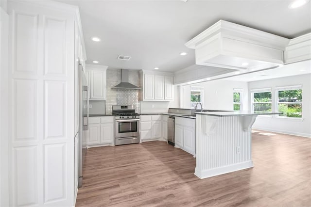 810 S Lahoma Ave, Norman, OK 73069 - kitchen with appliances with stainless steel finishes, wall chimney range hood, a peninsula, backsplash, and white cabinetry
