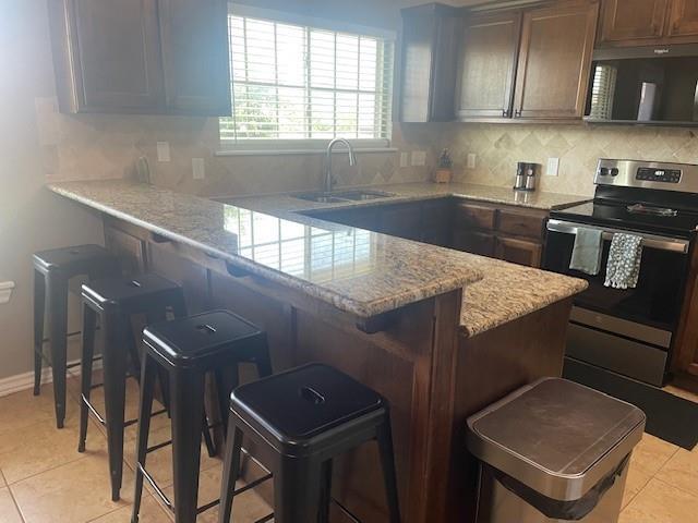 11820 SW 8th St, Yukon, OK 73099 - kitchen featuring electric range, a peninsula, a breakfast bar, decorative backsplash, and light tile patterned flooring