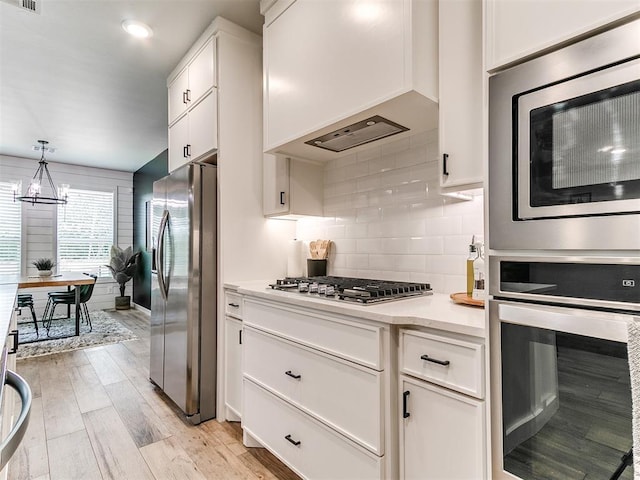 15109 Caspian Ln, Edmond, OK 73013 - kitchen with appliances with stainless steel finishes, custom range hood, white cabinets, decorative backsplash, and light wood-style floors