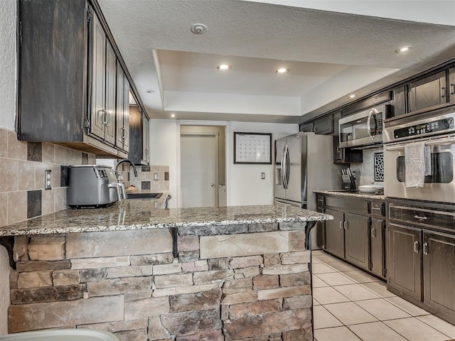 1008 S Neptune Rd, Edmond, OK 73003 - kitchen with appliances with stainless steel finishes, tasteful backsplash, a raised ceiling, light tile patterned floors, and dark brown cabinets