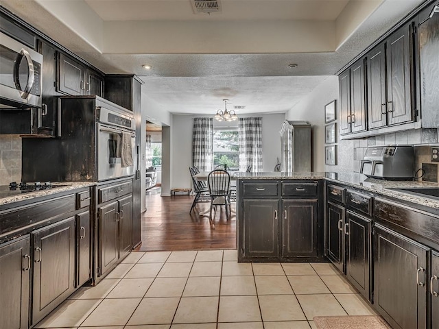 1008 S Neptune Rd, Edmond, OK 73003 - kitchen with stainless steel appliances, a chandelier, light tile patterned flooring, a peninsula, and decorative backsplash