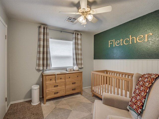 1008 S Neptune Rd, Edmond, OK 73003 - bedroom featuring a wainscoted wall, a crib, a textured ceiling, and ceiling fan