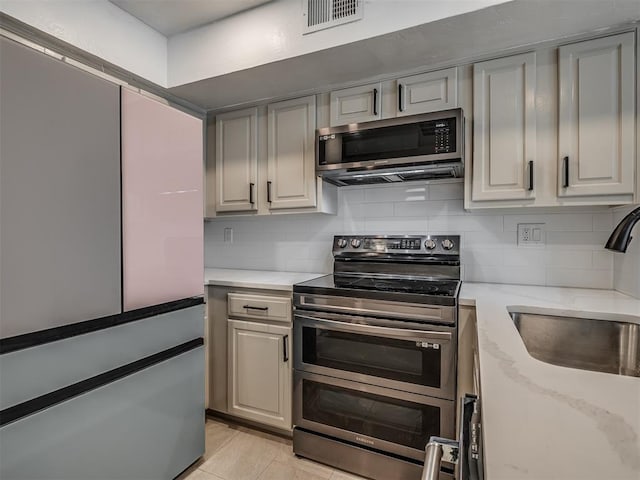 11550 N May Ave Unit 108, Oklahoma City, OK 73120 - kitchen with freestanding refrigerator, double oven range, decorative backsplash, light stone counters, and gray cabinetry