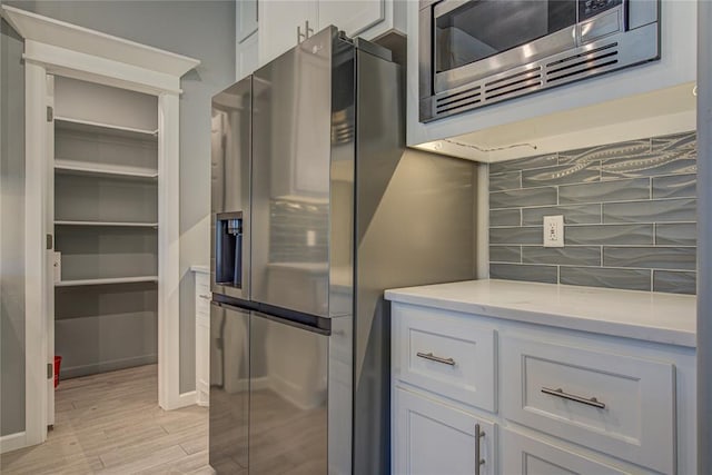 3800 Palmetto Trl, Oklahoma City, OK 73179 - kitchen with appliances with stainless steel finishes, light wood-style flooring, decorative backsplash, light stone counters, and white cabinets