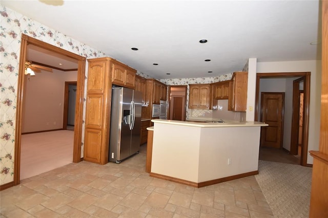 12608 Redstone Ct, Oklahoma City, OK 73142 - kitchen with stainless steel fridge, wallpapered walls, a peninsula, brown cabinetry, and light stone finish flooring