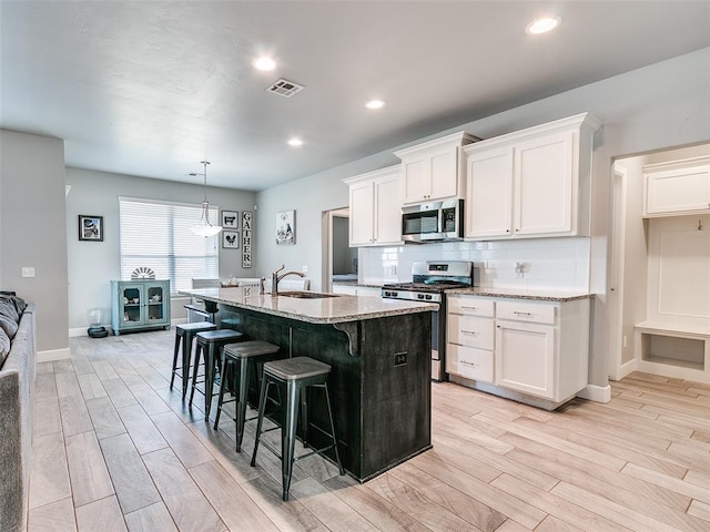 1417 Atalon Dr, Moore, OK 73160 - kitchen featuring appliances with stainless steel finishes, wood tiled floors, light stone counters, a breakfast bar, and an island with sink