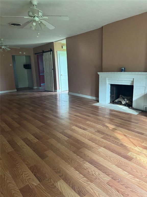 201 S Oak St, Pauls Valley, OK 73075 - unfurnished living room with ceiling fan, a barn door, wood finished floors, and a fireplace