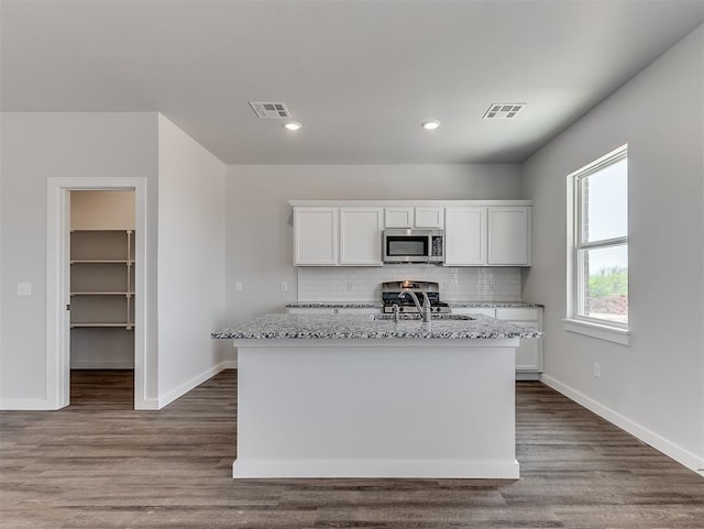 13172 Mannington Rd, Edmond, OK 73025 - kitchen featuring stainless steel microwave, light stone counters, decorative backsplash, white cabinetry, and a center island with sink