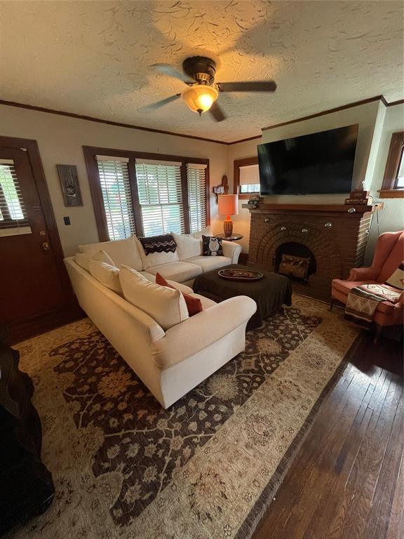 1845 W Park Pl, Oklahoma City, OK 73106 - living area featuring ornamental molding, wood finished floors, healthy amount of natural light, a ceiling fan, and a brick fireplace