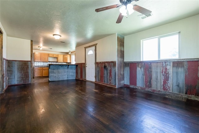 22807 E 1070th Rd, Clinton, OK 73601 - unfurnished living room featuring dark wood finished floors, a wainscoted wall, a ceiling fan, and wooden walls