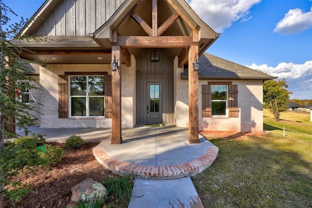 13337 SE 95th St, Oklahoma City, OK 73165 - view of exterior entry with brick siding, a patio area, a lawn, a shingled roof, and board and batten siding