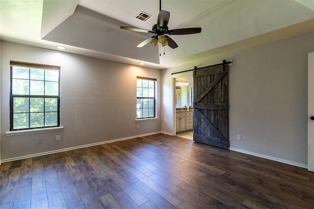 10517 SE 49th St, Oklahoma City, OK 73150 - unfurnished bedroom featuring a barn door, dark wood-style flooring, a raised ceiling, connected bathroom, and ceiling fan