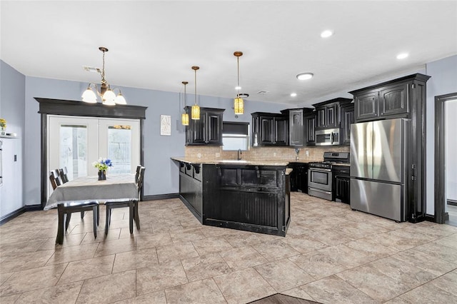 5901 NE Watts Rd, Elgin, OK 73538 - kitchen featuring appliances with stainless steel finishes, dark cabinetry, tasteful backsplash, a chandelier, and a peninsula