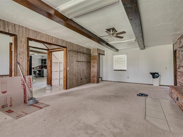 356818 E 1070th Rd, Prague, OK 74864 - unfurnished living room featuring a ceiling fan, beam ceiling, wood walls, carpet floors, and a textured ceiling