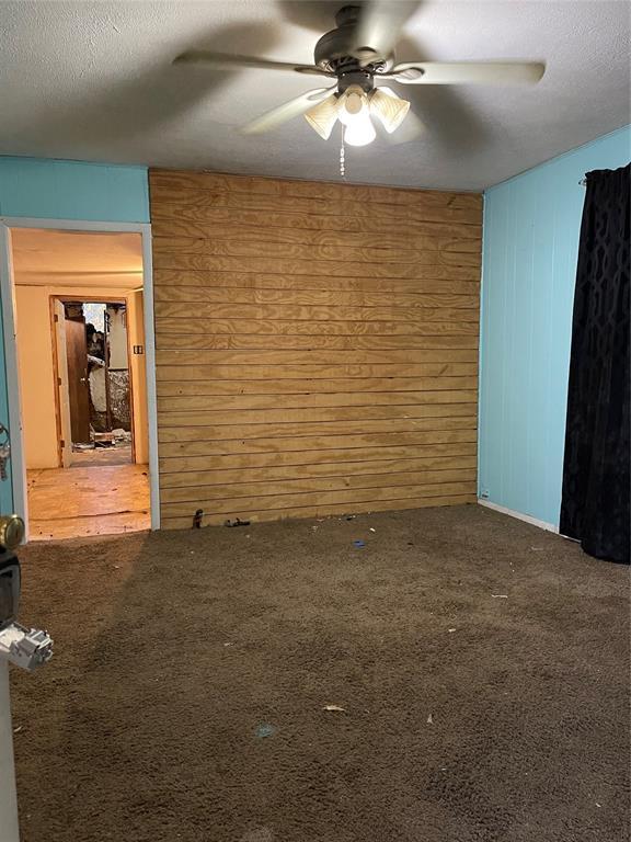 1309 W Pecan Ave, Duncan, OK 73533 - spare room featuring wooden walls, a ceiling fan, carpet floors, and a textured ceiling