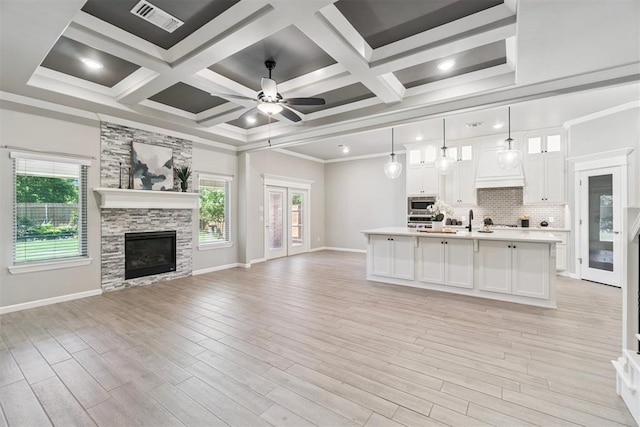 12904 SW 8th St, Yukon, OK 73099 - unfurnished living room featuring plenty of natural light, a ceiling fan, a stone fireplace, coffered ceiling, and light wood-type flooring