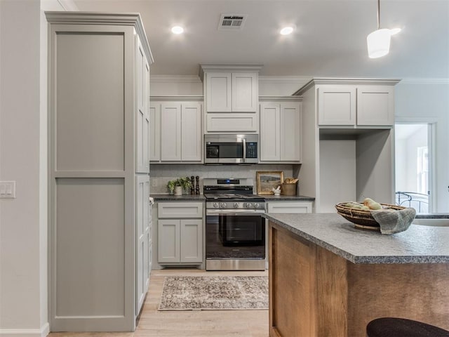 11728 SW 14th St, Yukon, OK 73099 - kitchen featuring appliances with stainless steel finishes, dark countertops, light wood-type flooring, crown molding, and decorative light fixtures