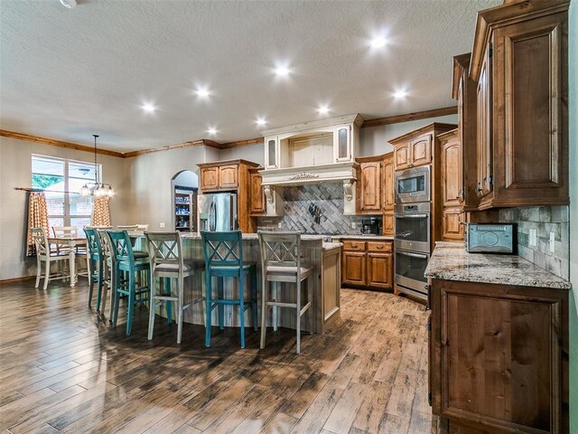 12905 S Mustang Rd, Mustang, OK 73064 - kitchen featuring appliances with stainless steel finishes, crown molding, a center island, a kitchen bar, and arched walkways