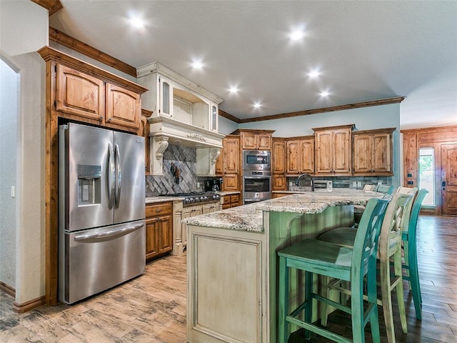 12905 S Mustang Rd, Mustang, OK 73064 - kitchen with appliances with stainless steel finishes, decorative backsplash, light wood-type flooring, light stone counters, and a kitchen breakfast bar