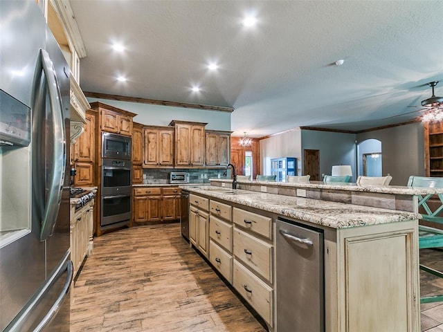 12905 S Mustang Rd, Mustang, OK 73064 - kitchen with appliances with stainless steel finishes, a center island with sink, light stone countertops, a ceiling fan, and wood finished floors