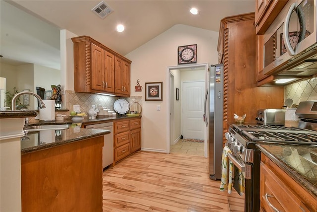 2221 NW 158th St, Edmond, OK 73013 - kitchen featuring stainless steel appliances, brown cabinetry, vaulted ceiling, backsplash, and dark stone counters