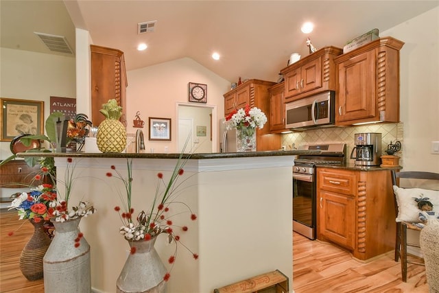 2221 NW 158th St, Edmond, OK 73013 - kitchen featuring stainless steel appliances, light wood-style floors, brown cabinetry, tasteful backsplash, and lofted ceiling