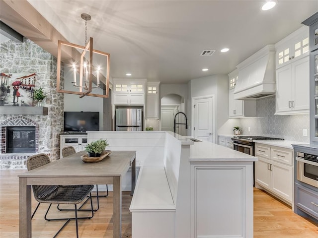 3508 Pavilion Pl, Edmond, OK 73034 - kitchen with arched walkways, appliances with stainless steel finishes, custom range hood, a large fireplace, and light countertops