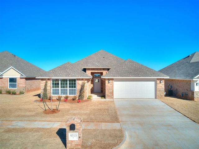 9313 NW 141st St, Yukon, OK 73099 - view of front of property featuring a garage, driveway, a shingled roof, and brick siding