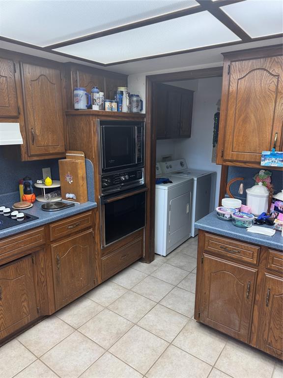 11700 Sierra Rd, Oklahoma City, OK 73162 - kitchen with black appliances, ventilation hood, independent washer and dryer, light tile patterned flooring, and dark countertops