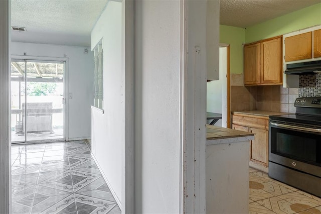 2120 E Robberts Ave, Kingfisher, OK 73750 - kitchen featuring stainless steel range with electric stovetop, under cabinet range hood, a textured ceiling, tile counters, and light tile patterned floors