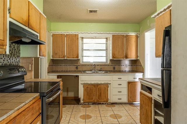 2120 E Robberts Ave, Kingfisher, OK 73750 - kitchen featuring black appliances, tile countertops, under cabinet range hood, decorative backsplash, and a textured ceiling