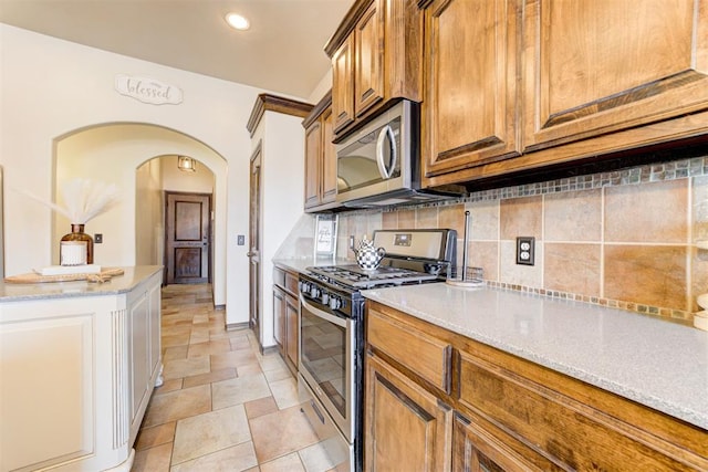 921 Tea Rose Dr, Yukon, OK 73099 - kitchen with appliances with stainless steel finishes, backsplash, arched walkways, brown cabinets, and light stone countertops