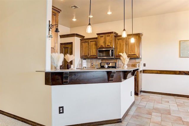 921 Tea Rose Dr, Yukon, OK 73099 - kitchen featuring stainless steel microwave, range, a kitchen bar, tasteful backsplash, and brown cabinetry