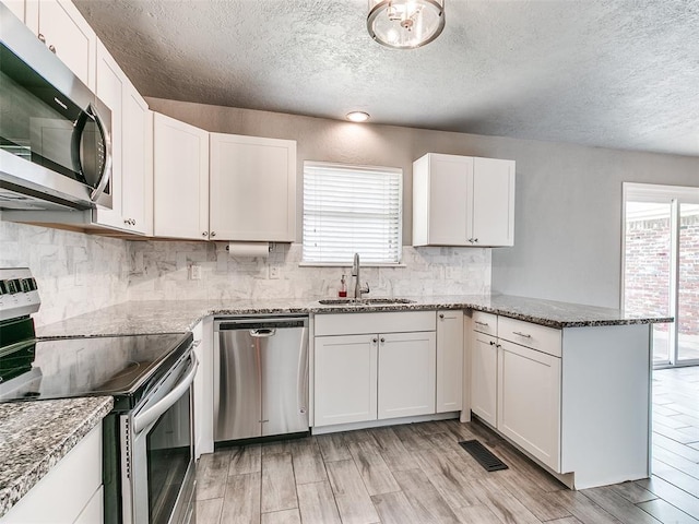 1917 Barryton Rd, Oklahoma City, OK 73120 - kitchen featuring stainless steel appliances, a textured ceiling, a peninsula, plenty of natural light, and white cabinetry