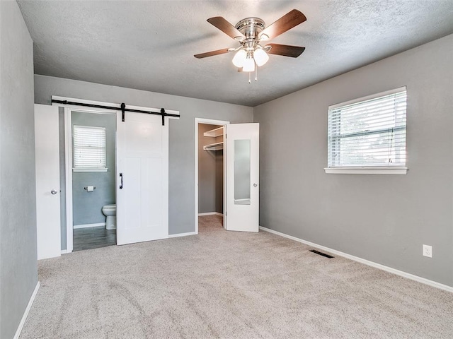 1917 Barryton Rd, Oklahoma City, OK 73120 - unfurnished bedroom featuring a barn door, a spacious closet, carpet flooring, a textured ceiling, and ensuite bathroom