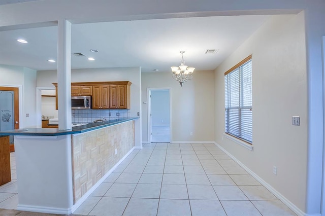4621 Deer Ridge Blvd, Yukon, OK 73099 - kitchen featuring stainless steel microwave, tasteful backsplash, brown cabinets, dark countertops, and a chandelier