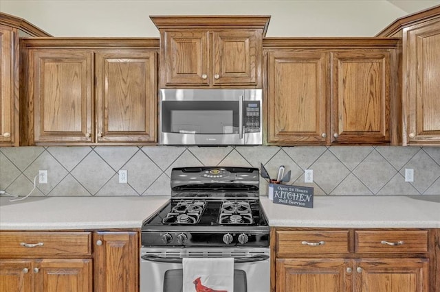 11321 NW 103rd St, Yukon, OK 73099 - kitchen featuring appliances with stainless steel finishes, brown cabinets, light countertops, and decorative backsplash