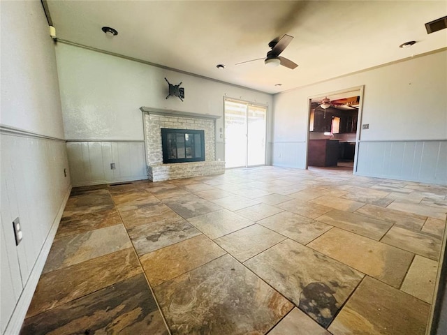 302 NE 60th St, Oklahoma City, OK 73105 - unfurnished living room featuring ceiling fan, a wainscoted wall, stone tile flooring, a fireplace, and a decorative wall