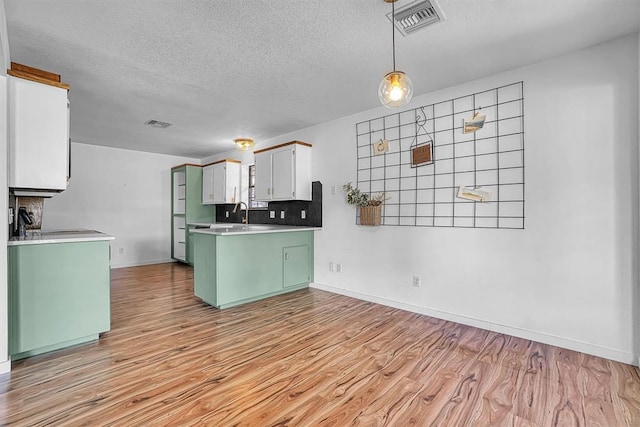 3208 Quail Cir, Altus, OK 73521 - kitchen with green cabinetry, a textured ceiling, light wood-style flooring, a peninsula, and light countertops