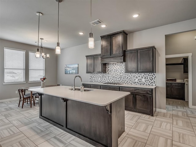 3903 Painted Bird Ln, Norman, OK 73071 - kitchen featuring dark brown cabinets, tasteful backsplash, light countertops, a kitchen island with sink, and recessed lighting