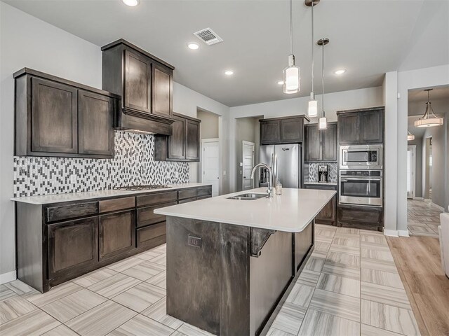 3903 Painted Bird Ln, Norman, OK 73071 - kitchen featuring stainless steel appliances, dark brown cabinets, light countertops, decorative backsplash, and a kitchen island with sink