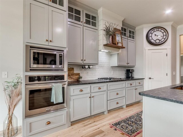 2209 Marjorie Ln, Yukon, OK 73099 - kitchen featuring appliances with stainless steel finishes, crown molding, tasteful backsplash, light wood-style flooring, and glass insert cabinets
