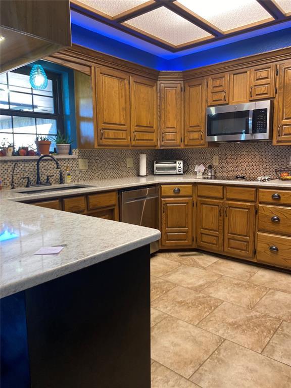 513 9th Street Cir, Hydro, OK 73048 - kitchen featuring stainless steel appliances, light countertops, brown cabinetry, and backsplash