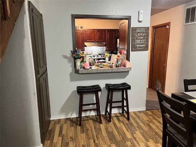 kitchen with under cabinet range hood, wood finished floors, a kitchen bar, and stainless steel range with electric cooktop