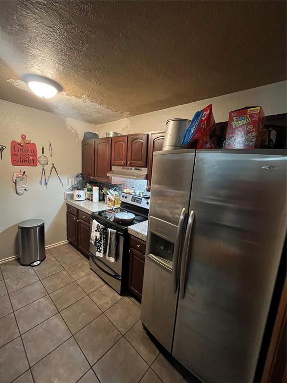 kitchen with stainless steel appliances, light tile patterned floors, light countertops, under cabinet range hood, and a textured ceiling