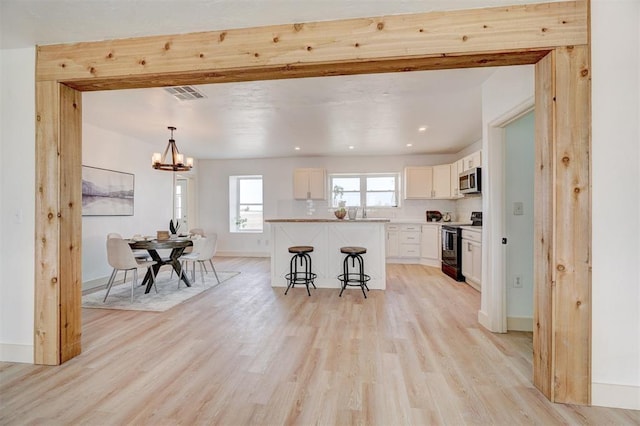 1646 County Road 1245, Tuttle, OK 73089 - kitchen with electric range, stainless steel microwave, a kitchen bar, light wood-style flooring, and white cabinets