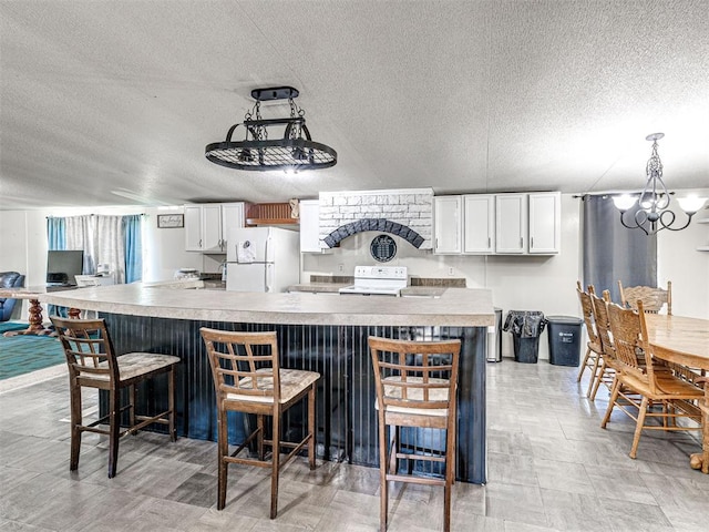 106411 Happy Trails Rd, Mcloud, OK 74851 - kitchen featuring a textured ceiling, freestanding refrigerator, a kitchen bar, white cabinetry, and a chandelier