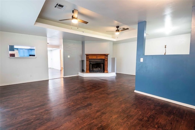 201 E 2nd St, Stroud, OK 74079 - unfurnished living room with a tray ceiling, ceiling fan, wood finished floors, and a fireplace with raised hearth