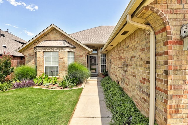10633 NW 38th St, Yukon, OK 73099 - view of exterior entry with brick siding, a lawn, and a shingled roof